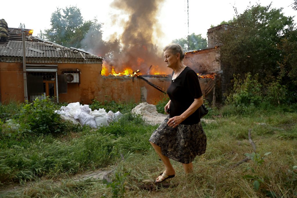 Donetsk'te bir bombalamanın ardından alev alan bir evden bir kadın kaçıyor.